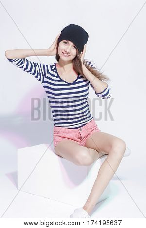 Youth fashion Concepts and Ideas. Stylish Smiling Caucasian Slim Brunette in Hat Posing On White Box in Studion Against White. Vertical Image Composition