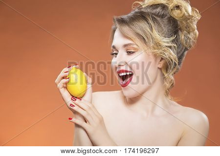 Sensual and Sexy Fruit Series. Positive Playful Caucasian Naked Girl Posing With Yellow Lemon Fruit. Against Orange Background.Horizontal Image