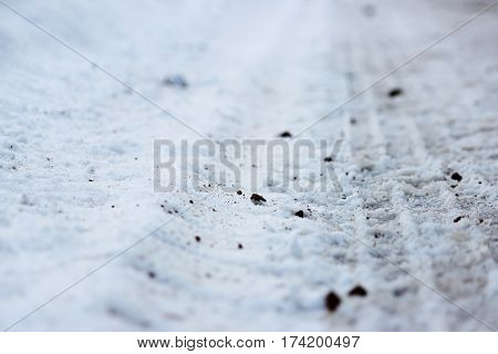 Footprints in the snow of the tractor, which threw sand on the road during icy
