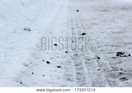 Footprints in the snow of the tractor, which threw sand on the road during icy