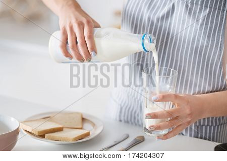 Light and fresh. Caring loving young mother preparing a breakfast while wearing an apron and fillip up a glass