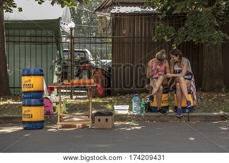 KIEV UKRAINE - AUGUST 9 2015: Young girls selling Kvass (a popular Eastern European drink) checking their smartphone on a street Kvass is a traditional Slavic and Baltic fermented beverage