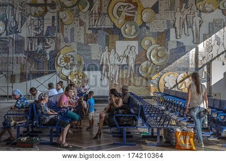 CHISINAU MOLDOVA - AUGUST 11 2015: People sitting in the waiting room of the Chisinau bus station waiting to board an intercity bus. A communist fresco can be seen in the background