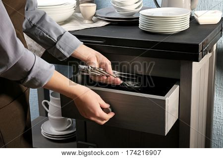 Woman putting silverware into drawer, closeup