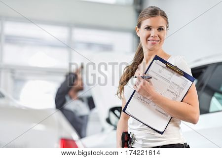 Portrait of smiling female repair worker with clipboard in car workshop