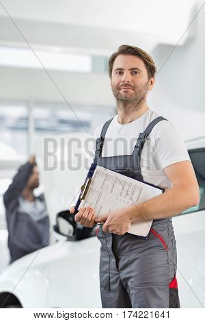 Portrait of confident male automobile mechanic with clipboard in car repair store