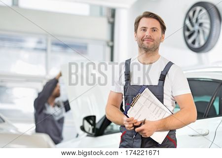 Portrait of confident male maintenance engineer with clipboard in car repair shop