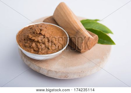 Ayurvedic Chandan powder or sandalwood paste in silver bowl with sticks and leaves placed over sahan or sahana or circular stone base for creating paste