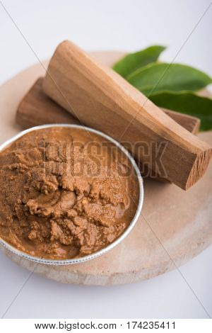 Ayurvedic Chandan powder or sandalwood paste in silver bowl with sticks and leaves placed over sahan or sahana or circular stone base for creating paste