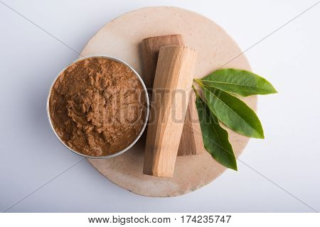 Ayurvedic Chandan powder or sandalwood paste in silver bowl with sticks and leaves placed over sahan or sahana or circular stone base for creating paste