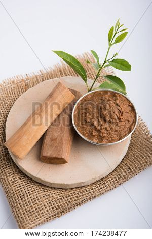 Ayurvedic Chandan powder or sandalwood paste in silver bowl with sticks and leaves placed over sahan or sahana or circular stone base for creating paste