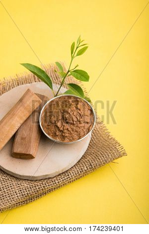 Ayurvedic Chandan powder or sandalwood paste in silver bowl with sticks and leaves placed over sahan or sahana or circular stone base for creating paste