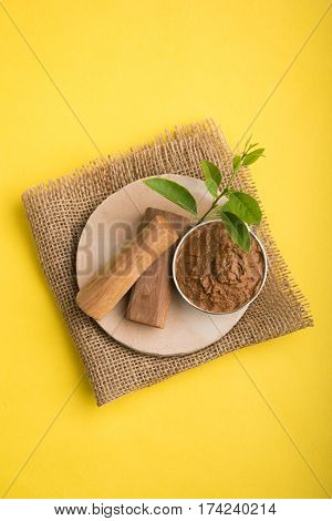 Ayurvedic Chandan powder or sandalwood paste in silver bowl with sticks and leaves placed over sahan or sahana or circular stone base for creating paste