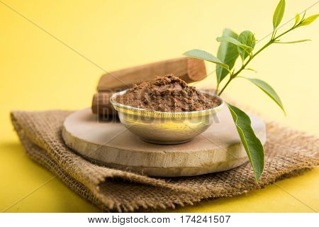 Ayurvedic Chandan powder or sandalwood paste in silver bowl with sticks and leaves placed over sahan or sahana or circular stone base for creating paste