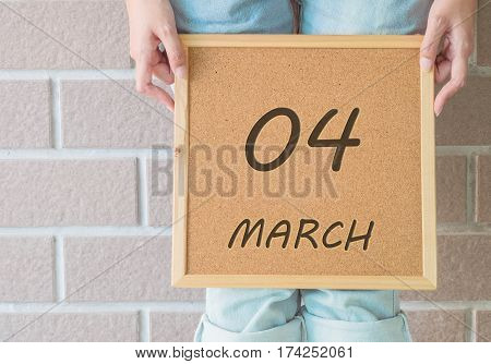 Closeup calendar at the cork board in hand of asian woman in front of her legs with 4 march word on brick wall textured background