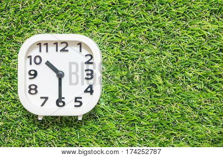 Closeup white clock for decorate show a half past ten or 10:30 a.m. on green artificial grass floor textured background with copy space