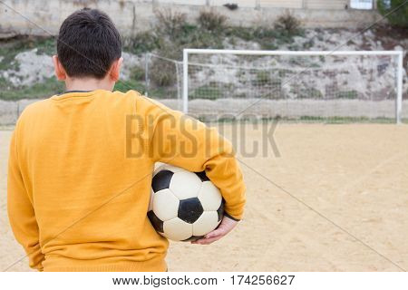 Sad boy waiting to play ball in an old soccer field
