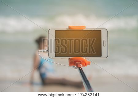 taking picture by smart phone selfie stick on blurred beautiful at beach background Vacation concept