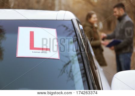 Learner driver sign on car windscreen. Blurred view of instructor and driver outdoors