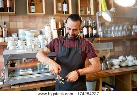 small business, people and service concept - happy man or waiter in apron with holder and tamper preparing espresso at coffee shop