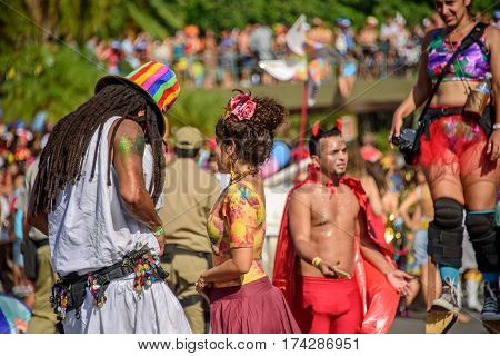 RIO DE JANEIRO, BRAZIL - FEBRUARY 28, 2017: Couple of man with dreadlocks and in colored tall hat and young woman on the background of blurry man in devil costume and woman walking on stilts