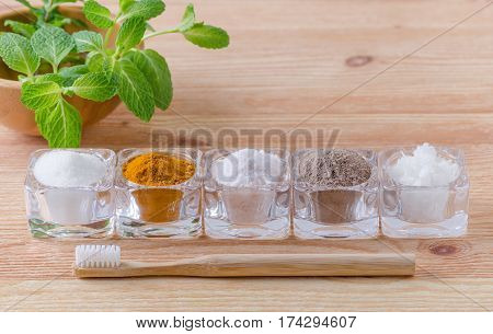 alternative natural toothpaste xylitol- soda turmeric - curcuma himalayan salt clay- ash coconut oil and wood toothbrush mint on wooden background