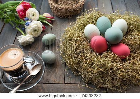 Still life with coffee and colorful easter eggs in a nest on a old shabby wooden table