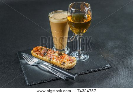 left side view on a tasty crispy bread with melted cheese pepperoni ham mushrooms red onion and tomato sauce with white wine in glass and coffee latte cutlery lunch set