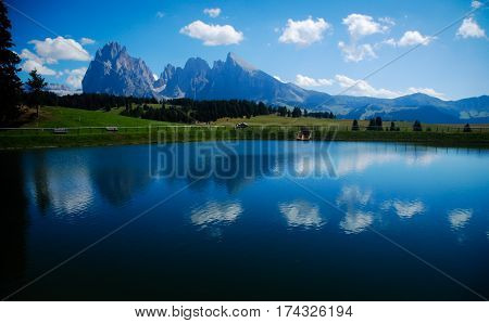 pond with reflection of dolomites mountains in italy on a blue sky background