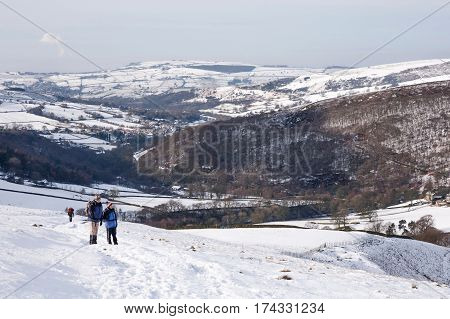 PEAK DISTRICT UK - CIRCA 2012: Senior couple hiking up Kinder Scout in winter snow. Hayfield Peak District UK