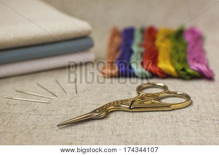 Embroidery and cross-stitch set on a natural linen background. Focus on the scissors.