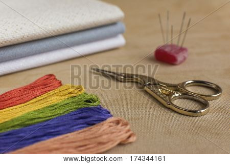 Cross-stitch kit for embroidery consisting of scissors needles multicoloured threads and canvas. Focus on the scissors.