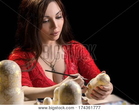 Young woman during the process of  painting handmade nested doll - russian matryoshka, dark background