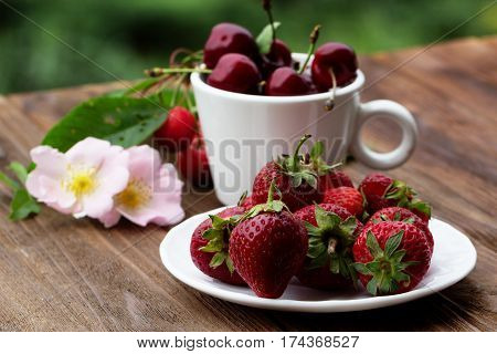 Group of fresh spring fruits together cherries and strawberries. Cherries in white bowl.Strawberry on a wooden background. Red strawberries. Strawberries on green