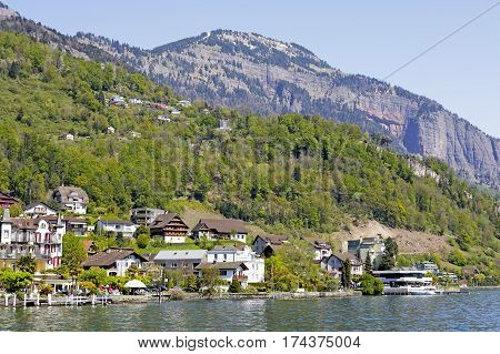 WEGGIS SWITZERLAND - MAY 05 2016: Houses by the Lake Lucerne can be seen on the background of mountains what creates mood of vacation. There are several people in a far distance.