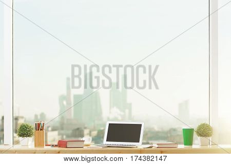 Front view of blank laptop computer placed on windowsill with book flowers supplies coffee cup and other items. Mock up. City view background