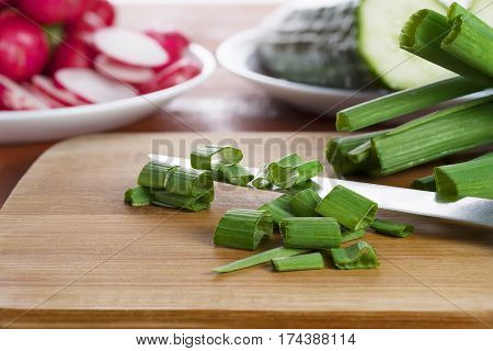 Young green onions cut by rings on a wooden board, prior to the treatment in lettuce