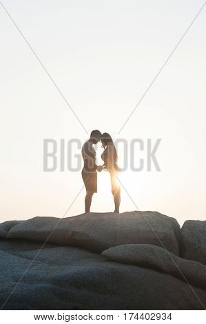 Lovely young adult couple standing on the rocks above tropical sea in isolated.
