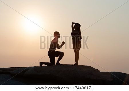 Lovely young adult couple standing on the rocks above tropical sea in Sunset.