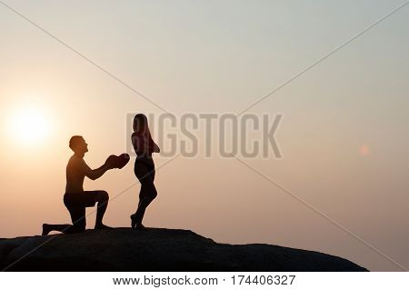 Lovely young adult couple standing on the rocks above tropical sea in Sunset.
