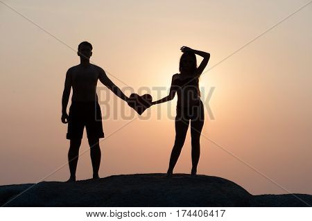 Lovely young adult couple standing on the rocks above tropical sea in Sunset.
