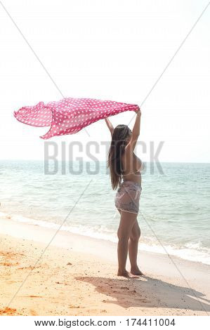 Positive pretty female holding fabric up and expressing gladness on the beach.