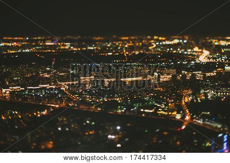 True tilt shift shooting of street surrounded by residential houses of night metropolis from very high point: warm lights from windows strong bokeh in background and foreground