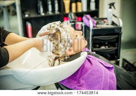 Hairdresser washing customer young woman meches head with professional shampoo and hair conditioner - People beauty care concept - Focus on head washed - Warm filter soft vignette