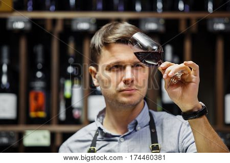 Bokal of red wine on background of male sommelier appreciating color, quality, flavor and sediments of drink. Professional degustation expert in winemaking.