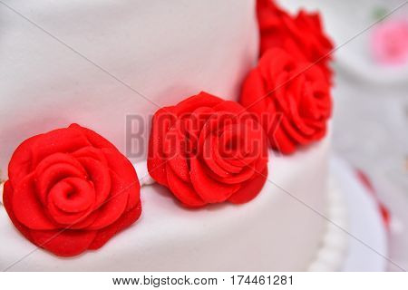 Sweet cakes in the form of red roses decorate the wedding cake with more decorative twigs of white cream. Photographed at a wedding in Novi Sad, Serbia.