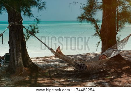 Bahamas beach with blue water man looking laying on hammock. Paradise vacation relaxing on hammock