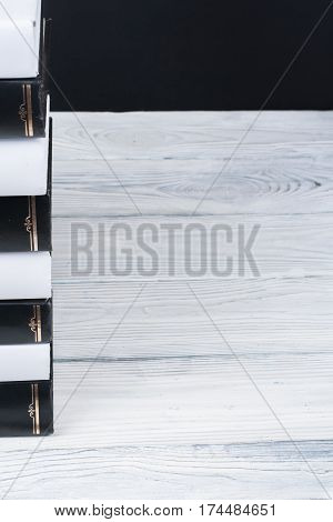 Spines of stacked hardback black and White books on wooden table. Back to school. Copy space for text. Education business concept
