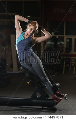 Woman doing strength exercises for abdominal muscles at indoor sport gym. Girl doing yoga stretches after running. Fitness model in dark sport club.