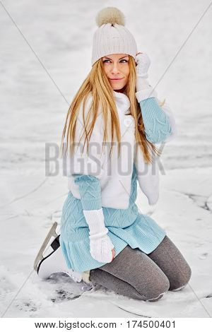 Young woman poses standing on knees at outdoor skate rink in winter park.